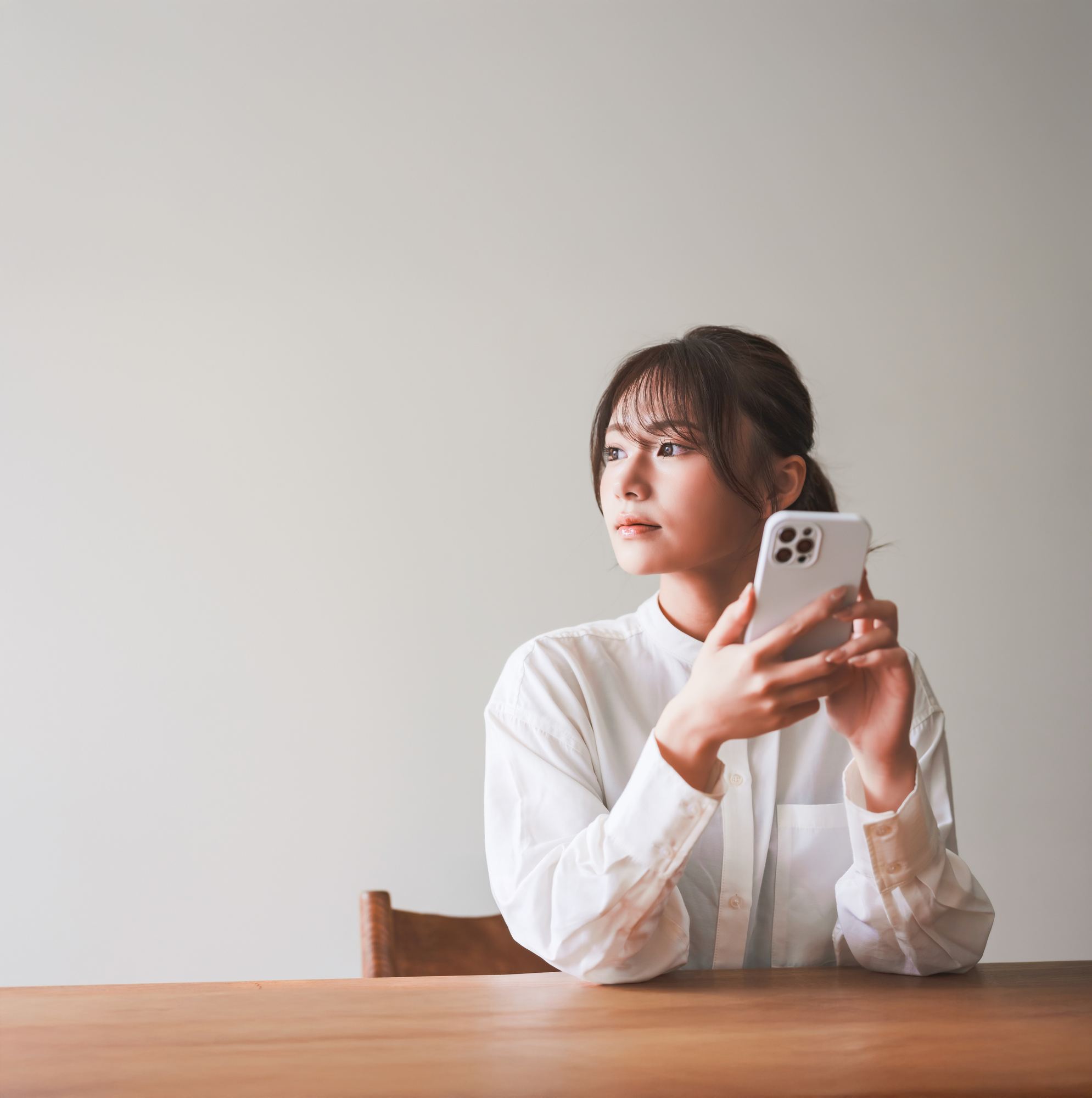 テーブルでスマートフォンを手に、考えごとをする人
